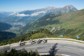 A large group of cyclists headed around a bend on road in the Alps.